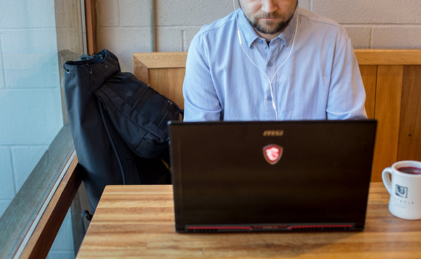 A person using their laptop at a cafe with the Original Shadow Guide 31 beside them.